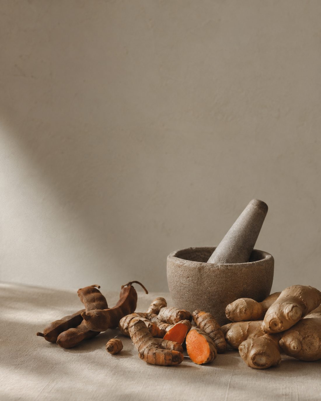 Turmeric, ginger and tamarind beside a stone mortar and pestle